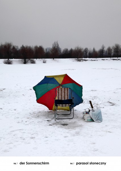 Rozległe, pokryte śniegiem pole, na środku: plażowe, skłądane krzesło pod kolorowym parasolem